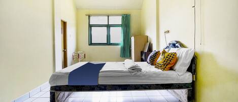 A single bed in a room with a window, a standing fan, and a door.