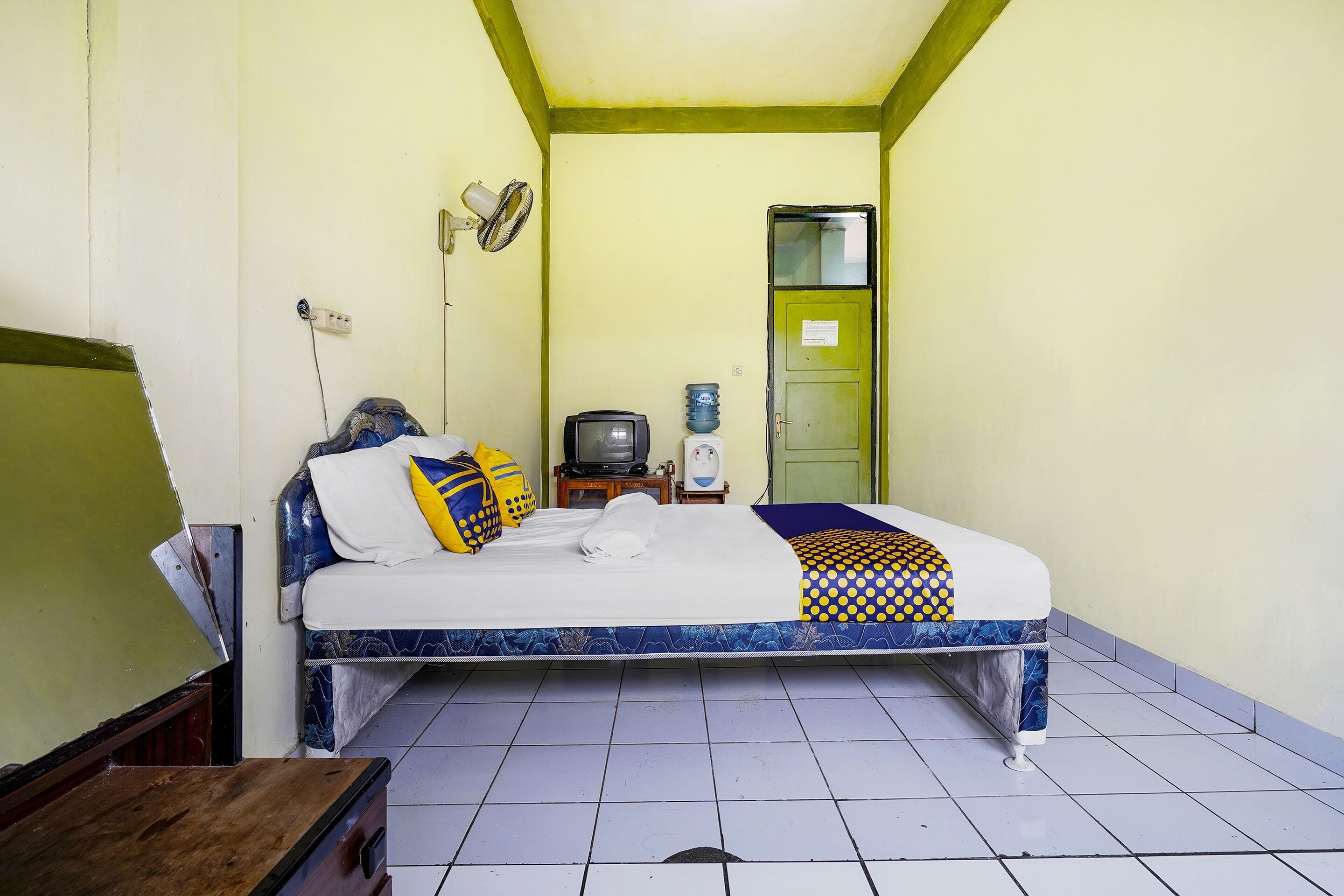 A small, simple room with a bed, a small table, a television, and a water dispenser.