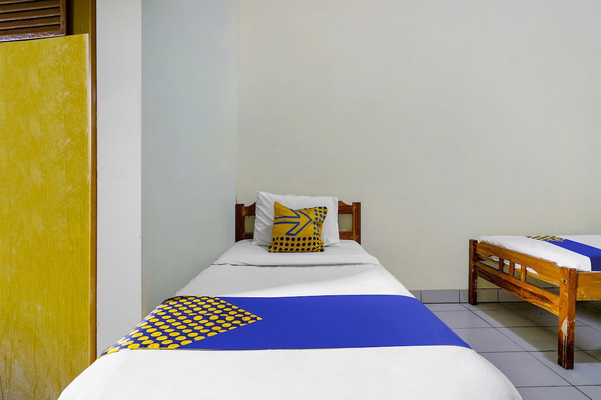 Uma cama de solteiro com colcha estampada em azul e amarelo, um travesseiro branco com desenho amarelo e cabeceira de madeira.