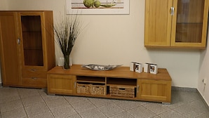 Ein Holzschrank mit Glastür, eine Vase mit Zweigen und ein gerahmtes Bild an der Wand.