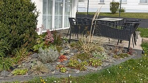 Eine Terrasse mit Gartenmöbeln, einem Kiesweg und verschiedenen Pflanzen.