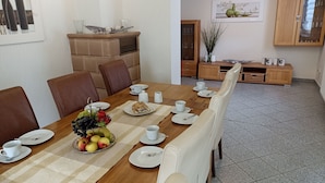Ein Essbereich mit einem langen Holztisch, gedeckt für sechs Personen, umgeben von Ledersesseln. Auf dem Tisch steht eine Obstschale, und im Hintergrund ist ein Schrank mit Glastüren zu sehen.