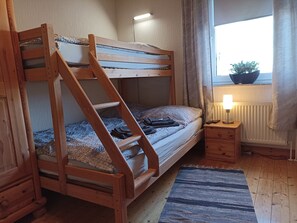Una cama litera con escalera de madera, una mesita de noche con lámpara, una ventana con vistas y un radiador.