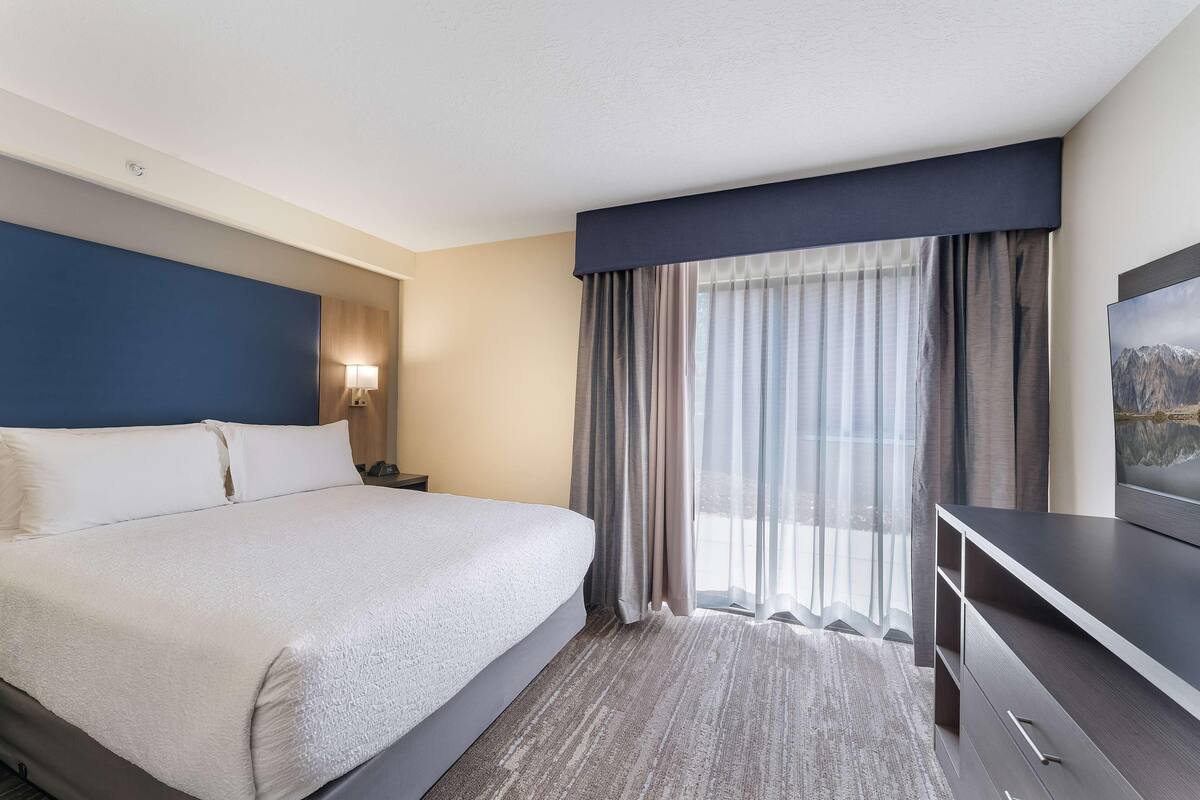 Une chambre d’hôtel avec un grand lit, un bureau et une fenêtre avec des rideaux.