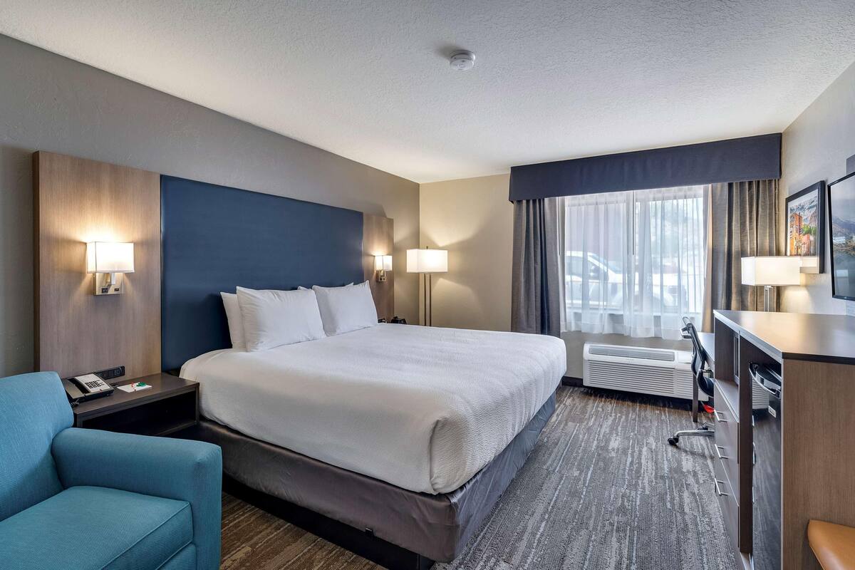 Une chambre d’hôtel avec un grand lit, un bureau, une chaise et une vue sur la rue par la fenêtre.