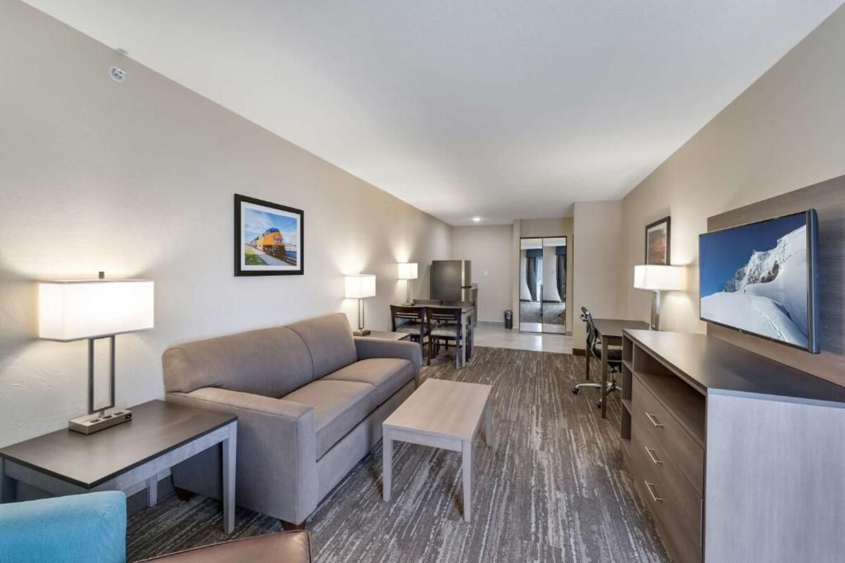 A hotel room with a sofa, a small table, a TV, a desk, and a chair.