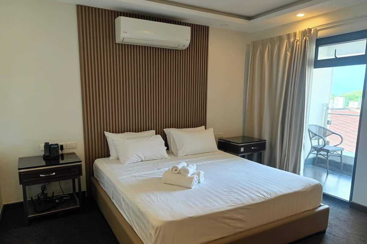Quarto de hotel com uma cama grande, mesa de cabeceira com telefone, aparelho de ar condicionado e vista para o exterior.