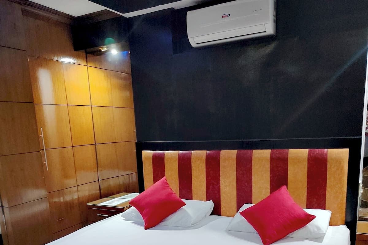 Quarto de hotel com cama, almofadas, cabeceira, unidade de ar condicionado e painéis de madeira.