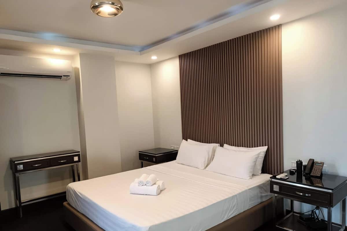 Quarto de hotel com cama, mesas de cabeceira, escrivaninha, aparelho de ar condicionado e telefone.