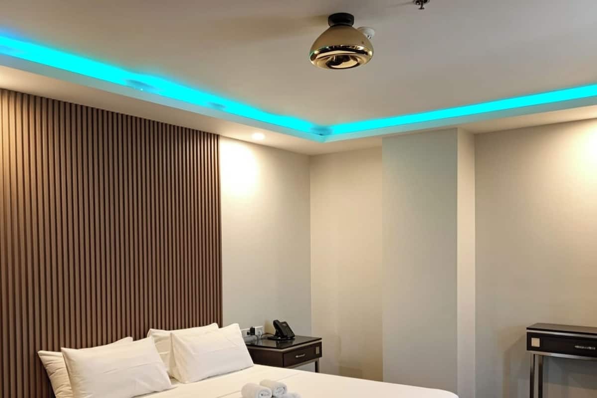 Quarto de hotel moderno com uma cama grande, mesas de cabeceira, escrivaninha e luminária no teto.
