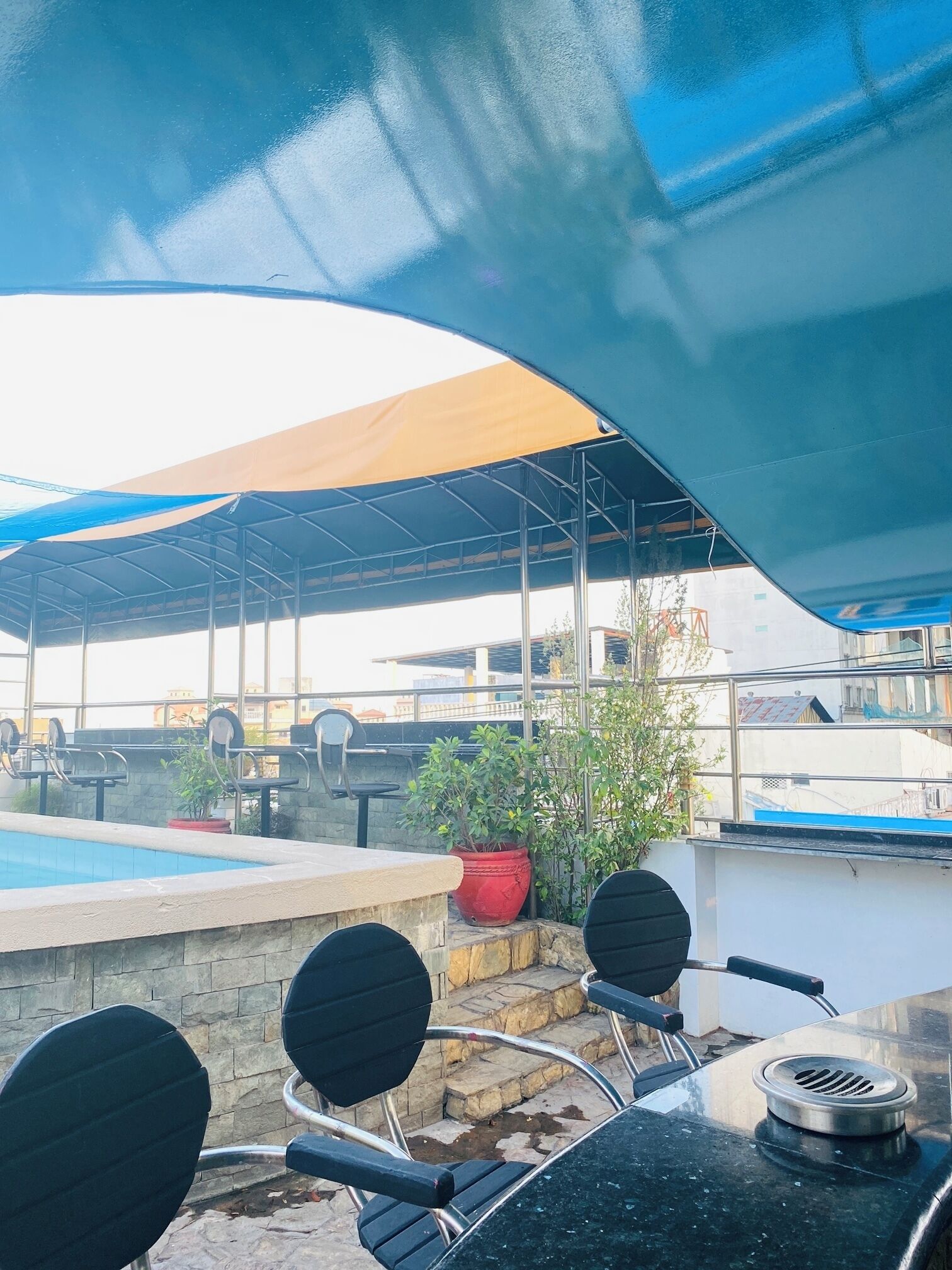 Un espace piscine extérieur doté d’un coin salon abrité, d’escaliers en pierre et de chaises en métal.