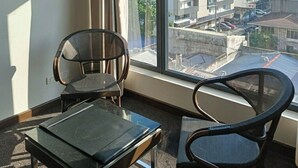 Habitació amb dues cadires, una taula petita i un finestral gran amb vista a la ciutat.