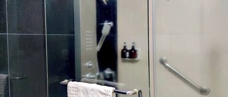 A modern bathroom with a glass shower enclosure, a towel rack, and a visible bottle of shampoo.