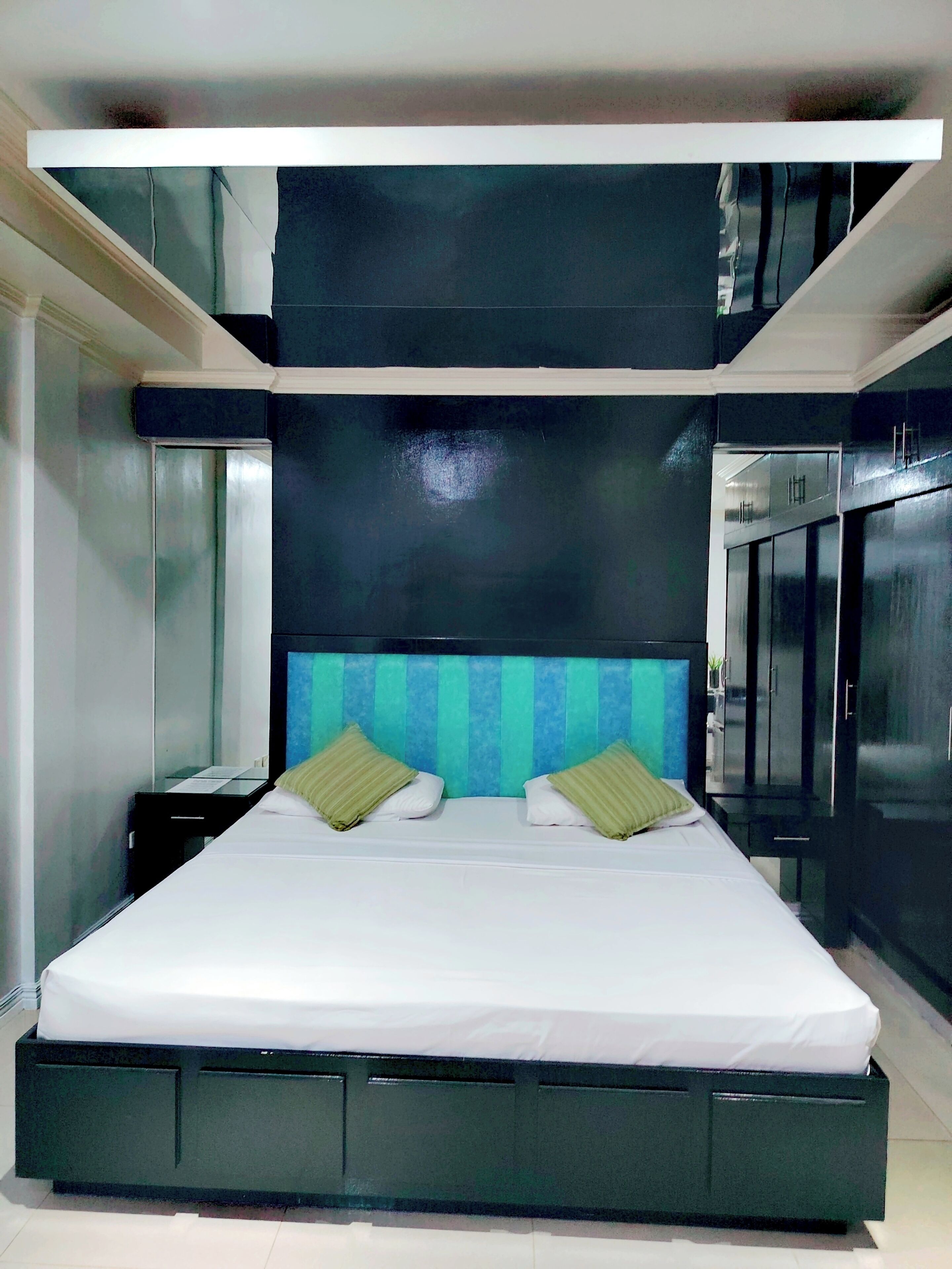 Una habitación de hotel moderna con una cama grande, una mesita de noche, un espejo y un armario.