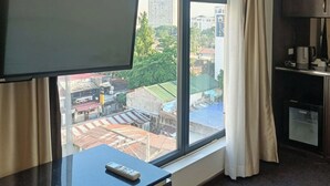 Habitació d'hotel amb una finestra gran, televisió de pantalla plana, comandament a distància sobre una taula, màquina de cafè i aire condicionat.