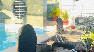 A poolside area with lounge chairs, a stone wall, and potted plants.