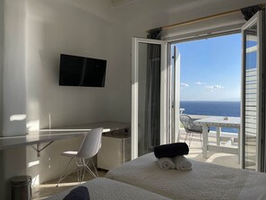 A hotel room with a bed, a desk, a chair, a TV, and a balcony with a view of the sea. - Studio 4 - Amazing sea view, shared pool and resort facilities (Mykonos)