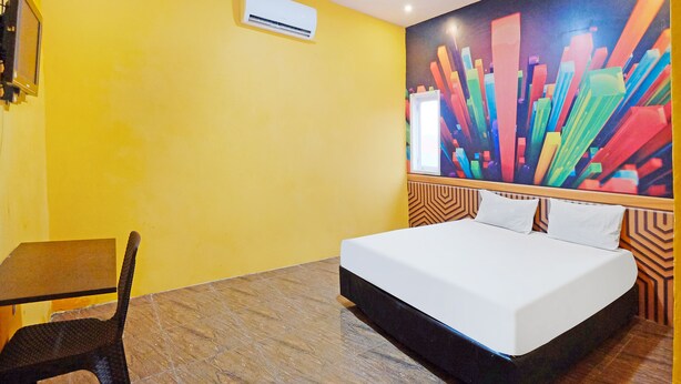 Una habitación de hotel con cama, una silla, una mesa y un cuadro abstracto y colorido en la pared.