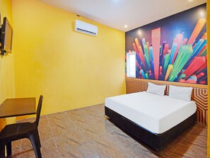 A hotel room with a bed, a chair, a desk, and a colorful abstract painting on the wall.