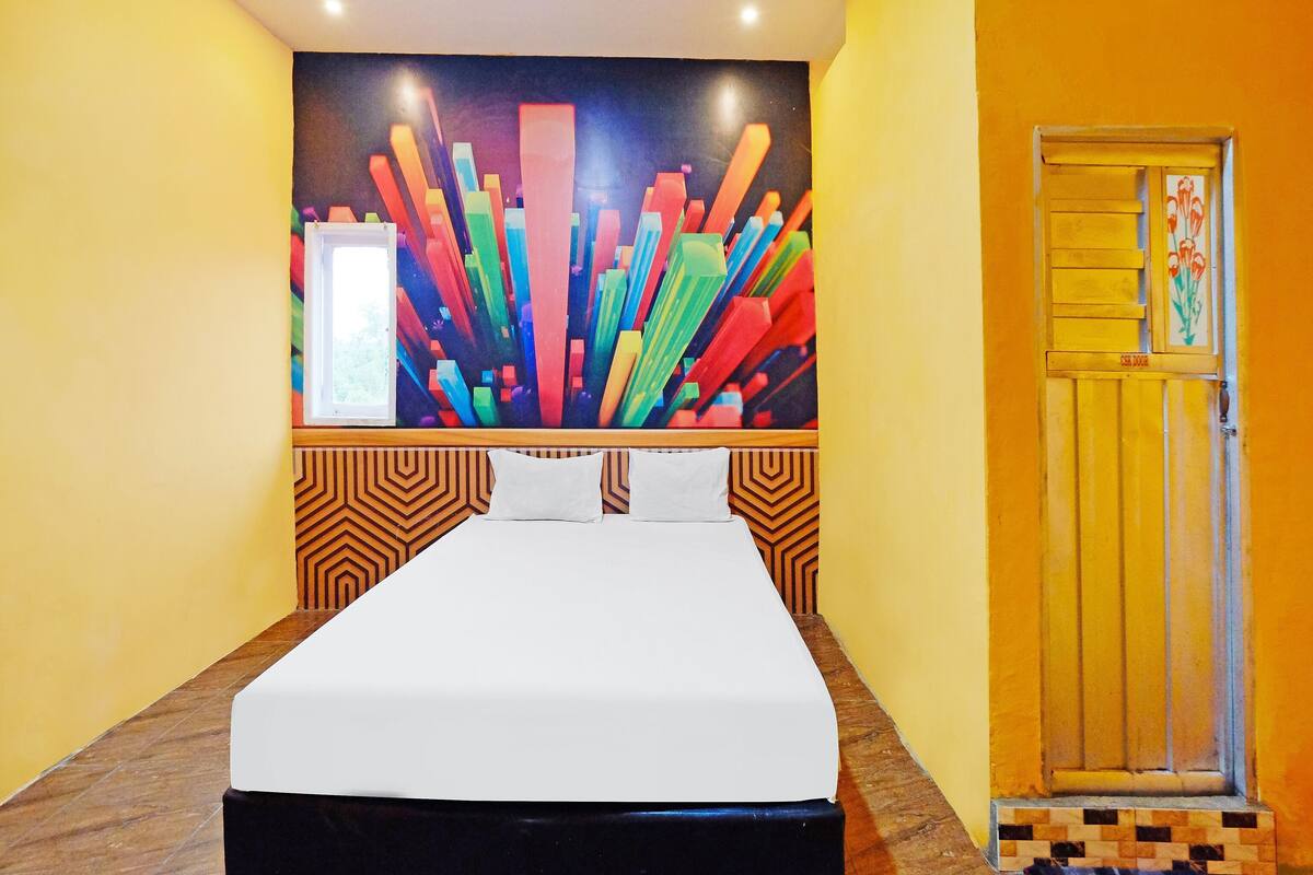 Una habitación de hotel con una cama, un cuadro abstracto y colorido en la pared, y una puerta con un diseño floral.