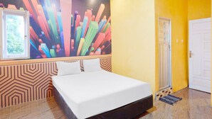 Habitación de hotel con cama, un mural abstracto de colores, una ventana que da a zonas verdes y una puerta.