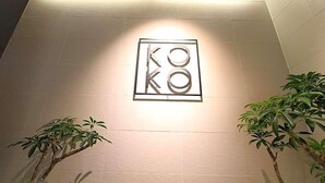 A wall-mounted sign with the letters "KO" in a modern font, flanked by two potted plants.