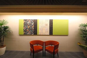 A waiting area with two orange chairs, a wall with three vertical panels, and potted plants on either side. - Koko Hotel Osaka Namba (Osaka)