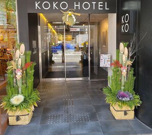 De ingang van KOKO HOTEL, met een modern design, voorzien van een glazen deur, een receptie en decoratieve planten.