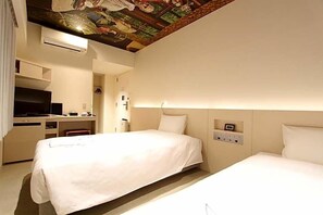 Een hotelkamer met twee bedden, een bureau, een televisie en een muurschildering aan het plafond.