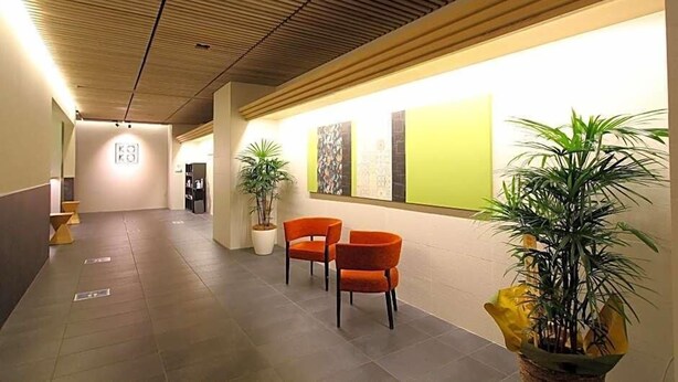 Een moderne hal met een houten plafond, potplanten en oranje stoelen.