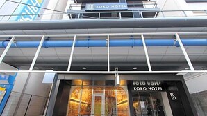 Een hotel met een moderne gevel, een opvallend bord met de tekst 'KOKO HOTEL' en een glazen ingang.