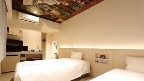 A hotel room with two beds, a desk, a television, and a ceiling mural.
