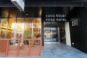 De ingang van Koko Hotel, met een moderne gevel en grote glasramen.