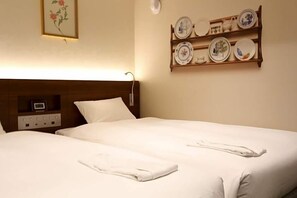Un lit bien fait, avec du linge de lit et des serviettes blanches, une table de chevet avec une horloge et une étagère murale avec des assiettes.