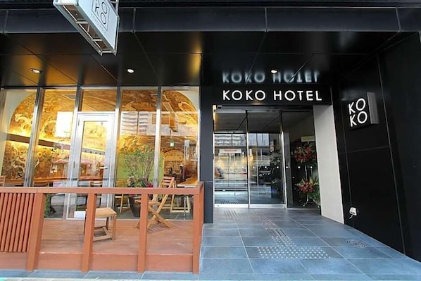 L’entrée de l’hôtel Koko, avec sa façade moderne et ses grandes fenêtres en verre.
