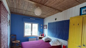 A room with a bed, a wooden wardrobe, a chair, a window, and a ceiling fan.
