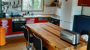 A kitchen with wooden cabinets, a wooden table, a toaster, and a window with a view of trees.