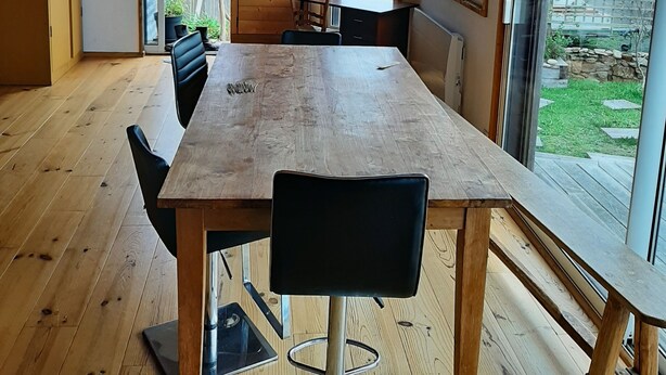 A spacious dining area with a large wooden table and black chairs, a wooden ceiling, and large windows offering a view of the outdoors.