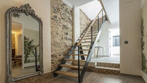 A staircase with a wooden finish and black metal railings, leading to a landing with a patterned floor and a stone wall. - Ayamonte Trajano Suites - Ayamonte Centre (Ayamonte)