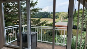 Ein Balkon mit Blick auf eine grüne Landschaft, ein Korbstuhl und eine Holzterrasse.