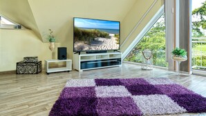 Ein modernes Wohnzimmer mit einem großen Flachbildfernseher, Holzböden und einem violett-weißen Teppich.