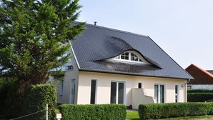 Ein eingeschossiges Haus mit geneigtem Dach, einer kleinen Veranda und einem gepflegten Rasen.