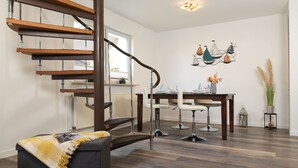 Un interior moderno con una escalera espiral de madera, un comedor con mesa y sillas, y una zona de estar acogedora con una manta.