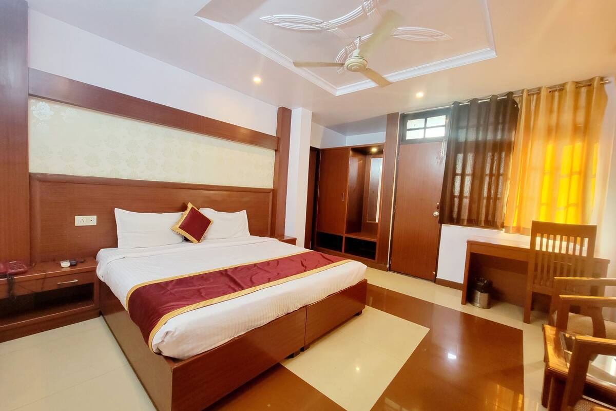 A hotel room with a bed, a desk, a chair, a wardrobe, and a ceiling fan.