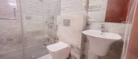 A modern bathroom with a glass shower enclosure, a white toilet, and a pedestal sink.