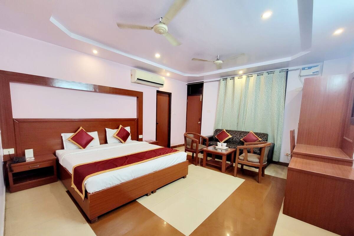 A hotel room with a large bed, two chairs, a small table, a ceiling fan, and an air conditioning unit.