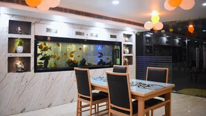Un comedor con un acuario grande, sillas de madera y una pared de mármol con estantes.