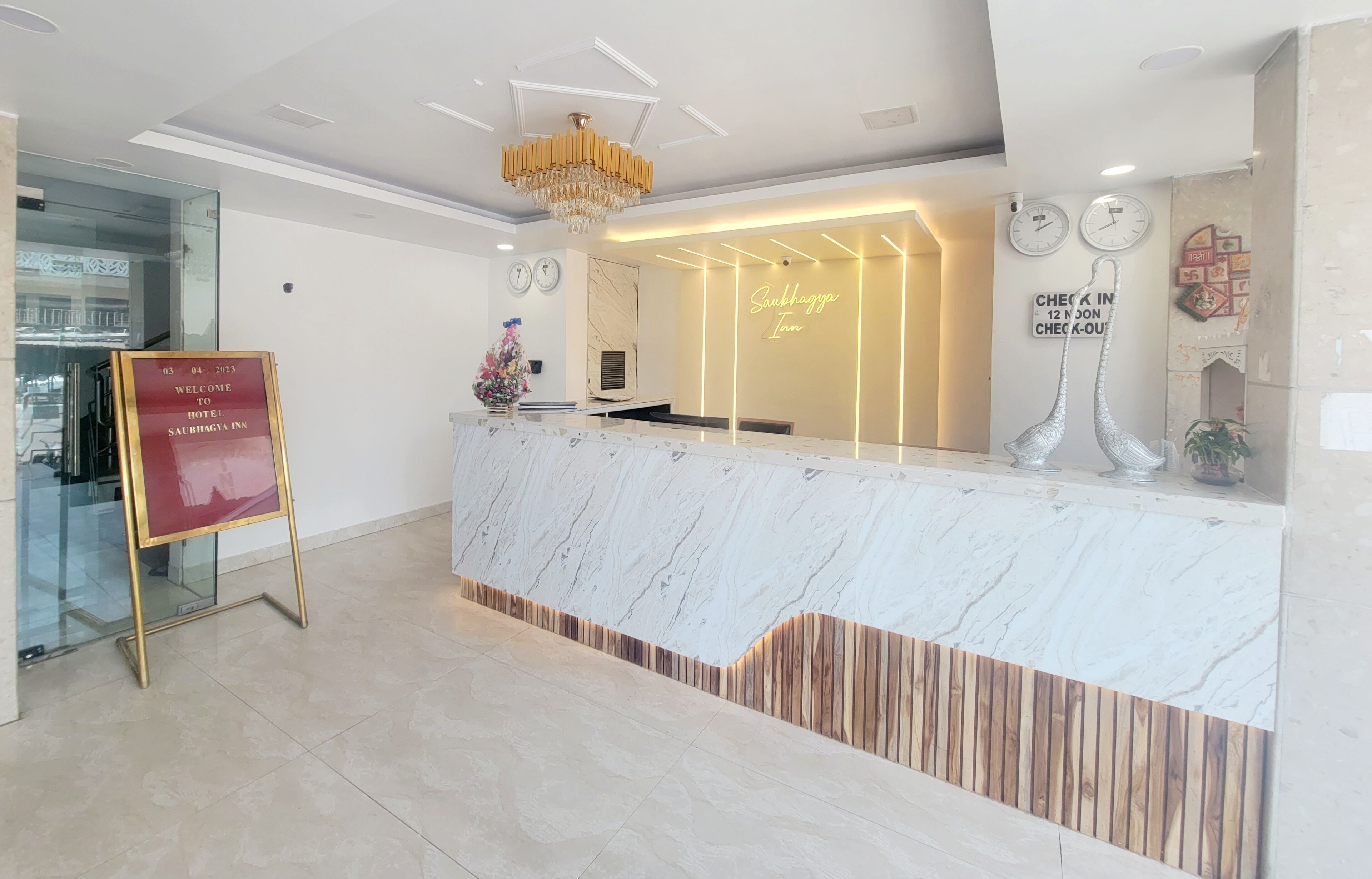 A hotel reception area with a marble counter, a chandelier, clocks, and a welcome sign.
