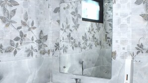 Un baño con un lavabo blanco, un espejo y un cubo de basura. Las paredes tienen un diseño de hojas.