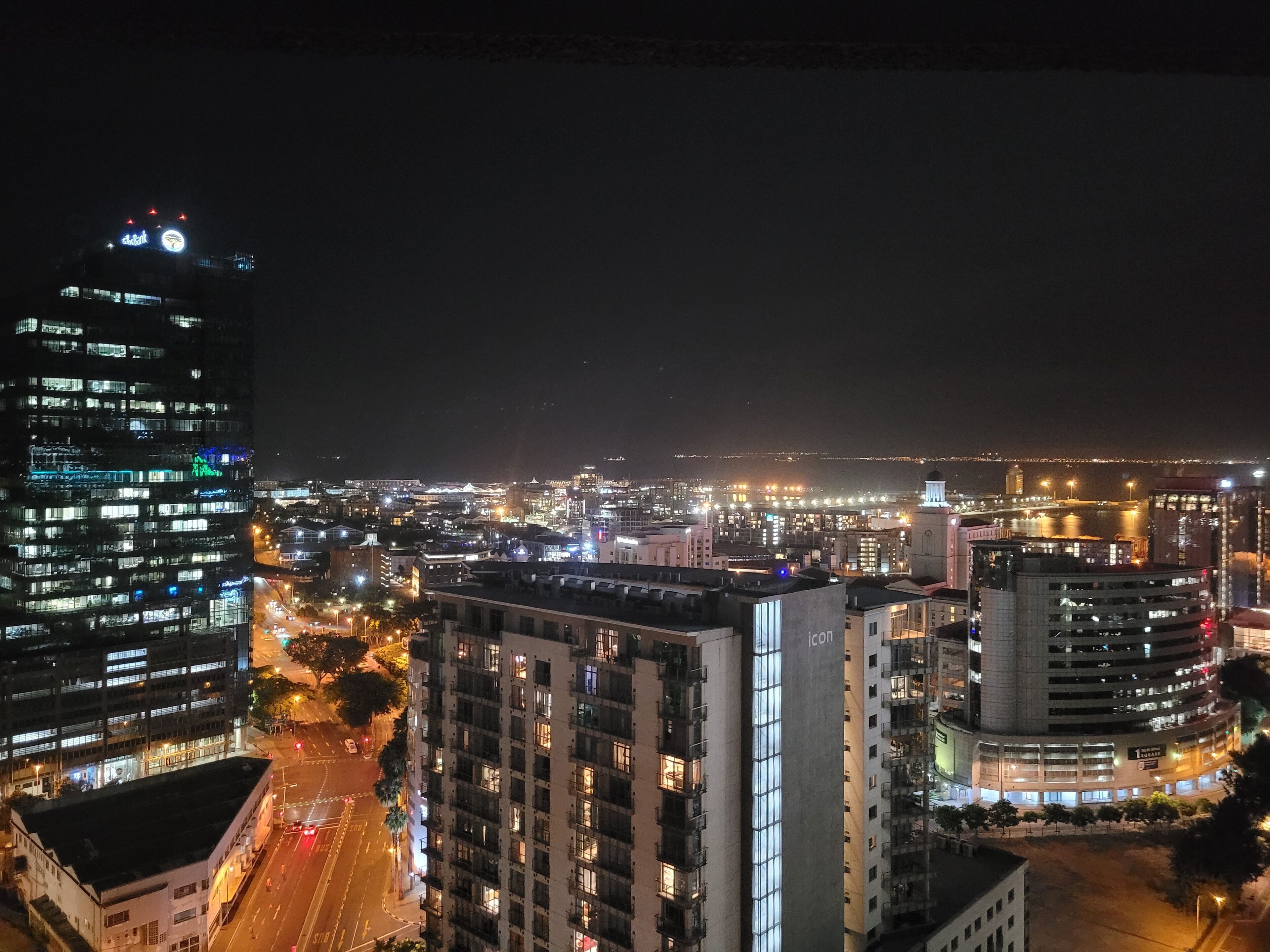 Une vue nocturne d’une ville, avec des bâtiments illuminés et une rivière en arrière-plan.